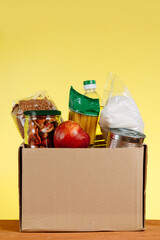 Food Donation concept. Donation Box With food For Donation On Yellow Backround. Assistance To The Elderly In The Context of The Coronavirus Pandemic. Vertical shot.