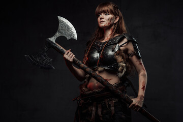 Brown haired grimy amazon from nord holding two handed axe and dressed in dark armour posing in...