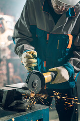 Locksmith in special clothes and goggles works in production. Metal processing with angle grinder....