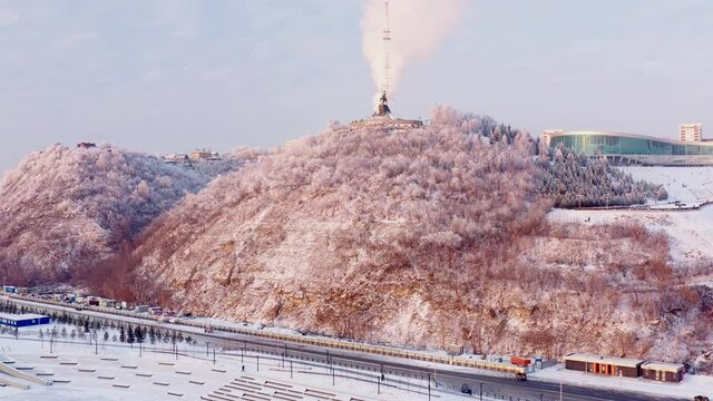 Aerial view of Winter hilly city with roads, trees, monument and buildings. Sunny cold winter day with beautiful cityscape. High quality 4k footage.