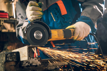 Locksmith in special clothes and goggles works in production. Metal processing with angle grinder....