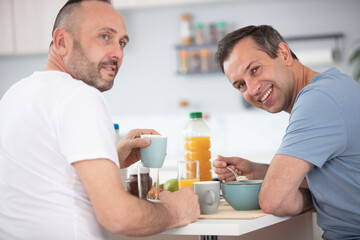 happy gay couple eating breakfast in kitchen