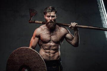 Furious medieval nord warrior with muscular build and naked torso posing in dark background holding...