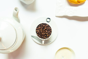 Coffee beans in a cup served. White composition with a tea pot, suggar and other elements as a concept of a break. Selective focus.