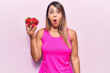 Young beautiful woman holding bowl with strawberries scared and amazed with open mouth for surprise, disbelief face