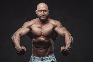 Fototapeta na wymiar Powerful and handsome bodybuilder with hairless head poses in dark background with naked torso with angry face looking at camera.
