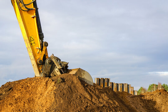 a yellow excavator boom with a bucket digs a pile of earth