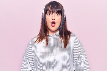 Young plus size woman wearing call center agent headset scared and amazed with open mouth for surprise, disbelief face