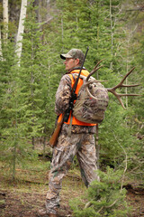 successful rifle hunter hiking through woods with deer in pack