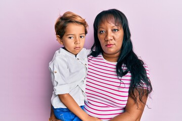 Hispanic family of mother and son hugging together with love thinking attitude and sober expression looking self confident