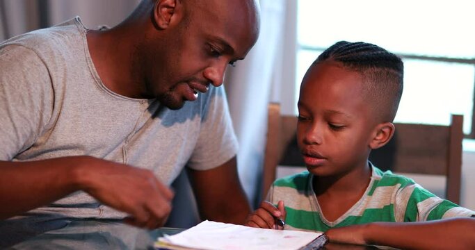 Little boy doing homework at home, African father helping son with study