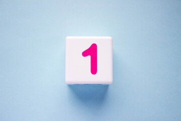 Close-up photo of a white plastic cube with a pink number one on a blue background. Object in the center of the photo