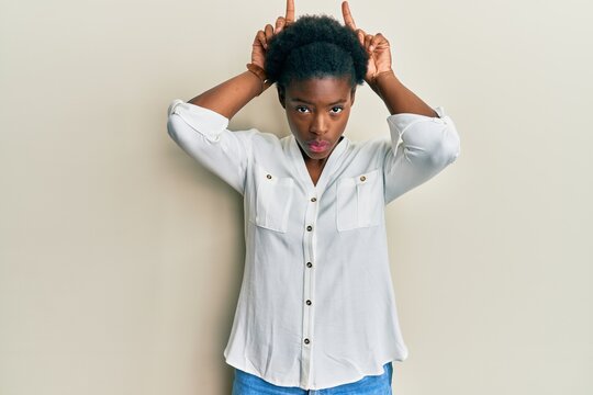 Young african american girl wearing casual clothes doing funny gesture with finger over head as bull horns