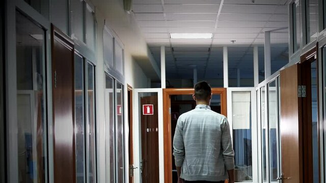 
a young man walks along the corridor of the office, lighting up light lamps. On the ceiling of the office corridor, lamps are switched on one by one.
