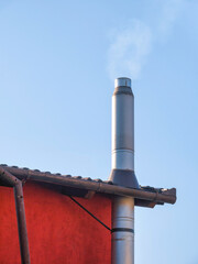 Metal tube pipe chimney on a house against blue sky.