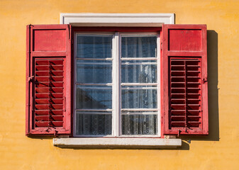 Obraz premium Detail of a window with old wooden shutters on a orange wall in medieval town of Sighisoara, Romania.