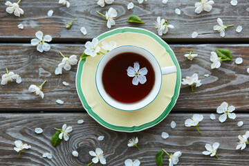 Obraz na płótnie Canvas A cup of tea on a wooden background covered with cherry flowers.