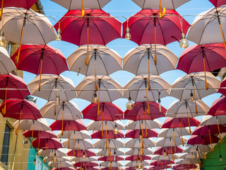 Fototapeta na wymiar Suspended colored umbrellas and light bulbs against blue sky.