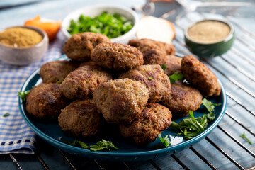 Minced meatball in dish with spices and parsley on wooden background. 