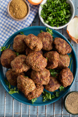 Minced meatball in dish with spices and parsley on wooden background. Top view.