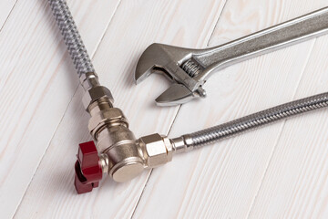 Braided flexible water hoses connected to an angle water tap. Adjustable wrench nearby. On white...
