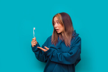 Obraz premium Girl in a blue sweatshirt with a toothbrush in her hand on a blue background. Close up studio portrait. Copy, empty space for text.