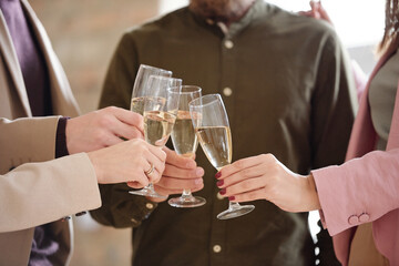 Hands of four young colleagues clinking with flutes of champagne during toast