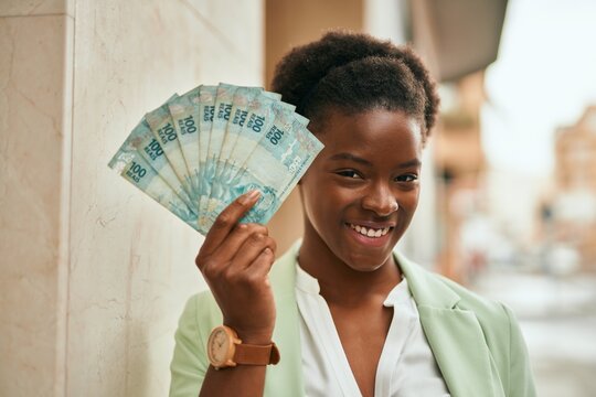 Young african american businesswoman smiling happy holding brazilian real banknotes at the city