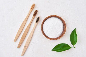 Three wooden bamboo toothbrushes and baking soda on white background, top view. Eco friendly toothbrushes, zero waste concept
