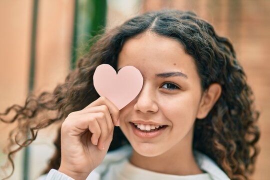Hispanic teenager girl smiling happy holding heart over eye at the city.