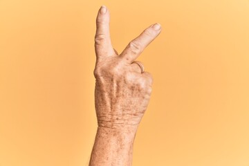 Senior caucasian hand over yellow isolated background counting number 2 showing two fingers, gesturing victory and winner symbol