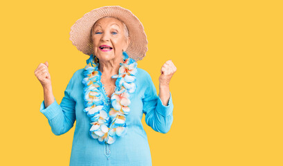 Senior beautiful woman with blue eyes and grey hair wearing summer hat and hawaiian lei screaming proud, celebrating victory and success very excited with raised arms - obrazy, fototapety, plakaty