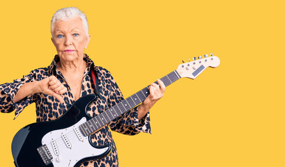 Senior beautiful woman with blue eyes and grey hair with modern look playing electric guitar with angry face, negative sign showing dislike with thumbs down, rejection concept