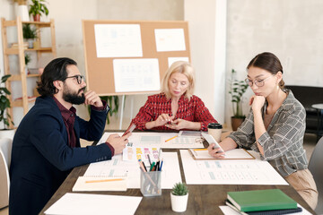 Three intercultural mobile application developers scrolling in smartphones