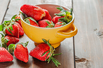 fragrant ripe strawberries in yellow ceramic bowl on a wooden surface