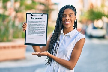 Young african american woman smiling happy holding clipboard with agreement document at the city.