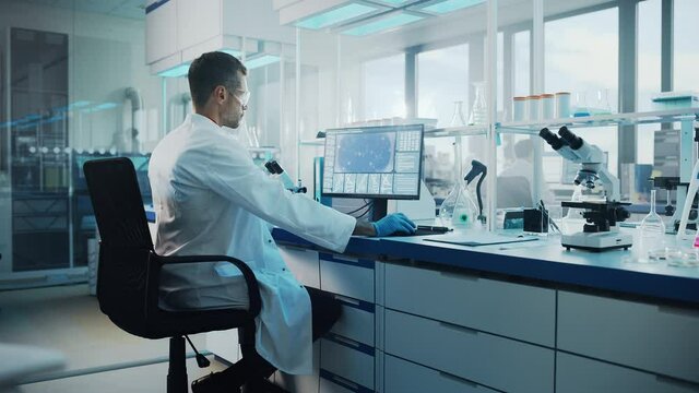 Medical Science Laboratory: Microbiologist Working on Computer with Display Showing Gene Editing Interface. Diverse Multi-Ethnic Team of Biotechnology Scientists Developing Drugs. Arc Zoom in Shot