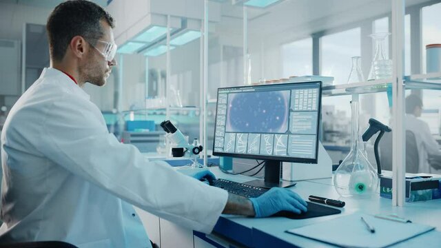 Medical Science Laboratory with Diverse Multi-Ethnic Team of Biotechnology Scientists Developing Drugs, Microbiologist Working on Computer with Display Showing Gene Editing Interface. Arc Zoom in Shot