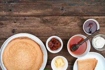 Ingredients for making pancakes, as well as ready-made pancakes on a brown background. Top view, with space to copy.