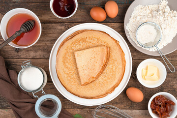Obraz na płótnie Canvas Flour, eggs, honey, sugar and a Stack of fried pancakes on a brown background. The view from the top. The concept of cooking, Mardi Gras.
