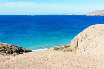 View of beautiful Playa Mujeres beach, blue sea, yellow sand, cliffs. Papagayo, Playa Blanca, Lanzarote, Canary Islands. VIew of Fuerteventura on the background, selective focus