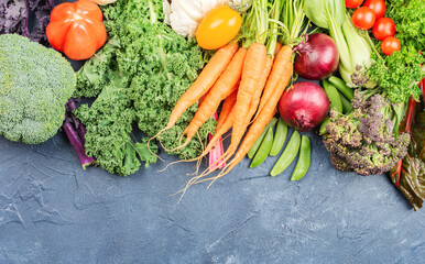 Variety of organic vegetables broccoli cauliflower carrots tomatoes kale pak choy onions. Healthy local farm produce on blue concrete table, top view, selective focus