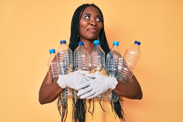 African american woman with braids holding recycling plastic bottles smiling looking to the side...