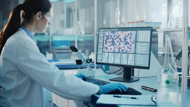 Medical Science Laboratory with Diverse Multi-Ethnic Team of Biotechnology Scientists Developing Drugs, Microbiologist Working on Computer with Display Showing Gene Editing Interface. Arc Dolly Shot