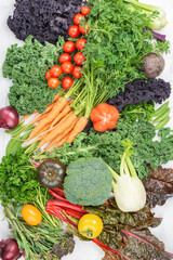 Variety of organic vegetables background, broccoli cauliflower carrots tomatoes kale pak choy onions chard. Healthy local farm produce on white wooden table, top view, selective focus