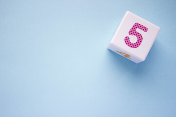 Close-up photo of a white plastic cube with a pink number 5 on a blue background in the upper right corner. With copy space