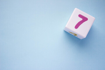 Photo of a white plastic cube with a purple number 7 on a blue background in the upper right...