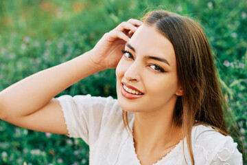 Fashion portrait of young woman resting on fresh green grass, wearing white dress