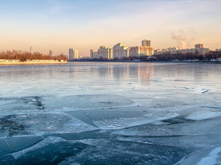 City skyline over a river covered with ice. Sunlight on a winter evening at sunset. View from the river embankment.