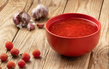 Tomato soup on a wooden table with cherry tomatoes and heads of garlic.